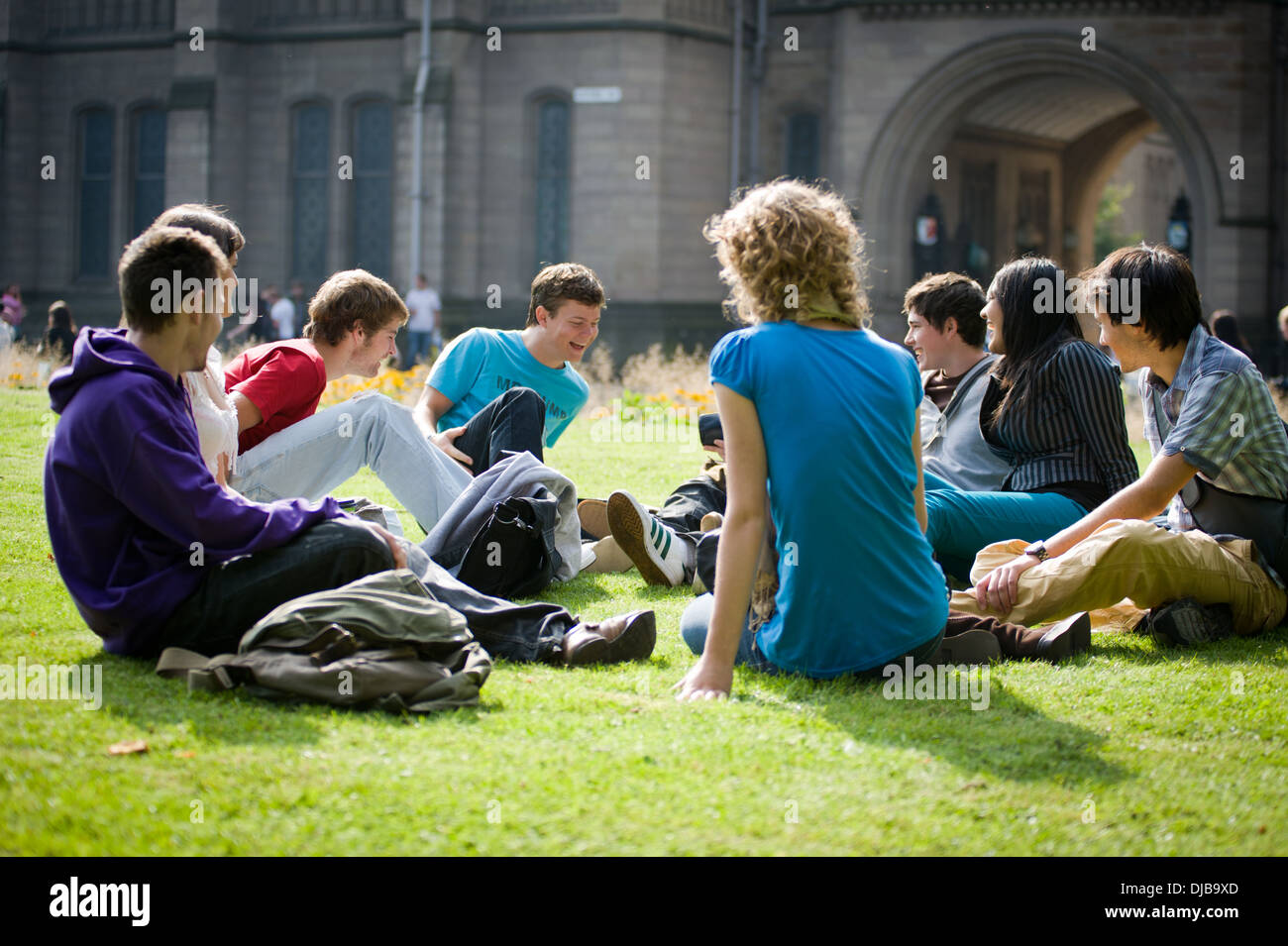Groupe d'étudiants de l'université de Manchester raciale multi assis sur l'herbe sur le campus dans la région de Sunshine parler et rire à heureux Banque D'Images