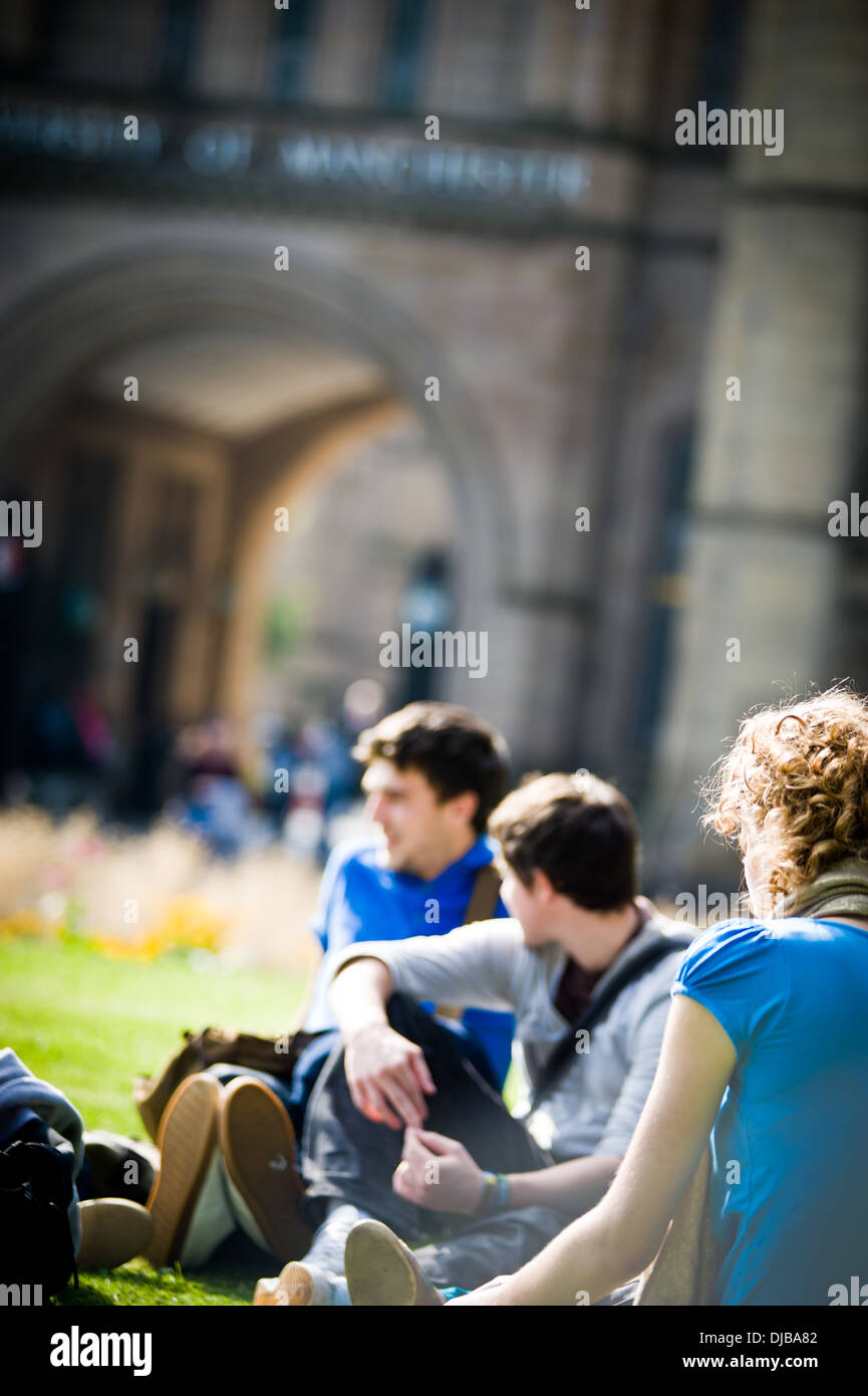 Groupe d'étudiants de l'université de Manchester raciale multi assis sur l'herbe sur le campus dans la région de Sunshine parler et rire à heureux Banque D'Images