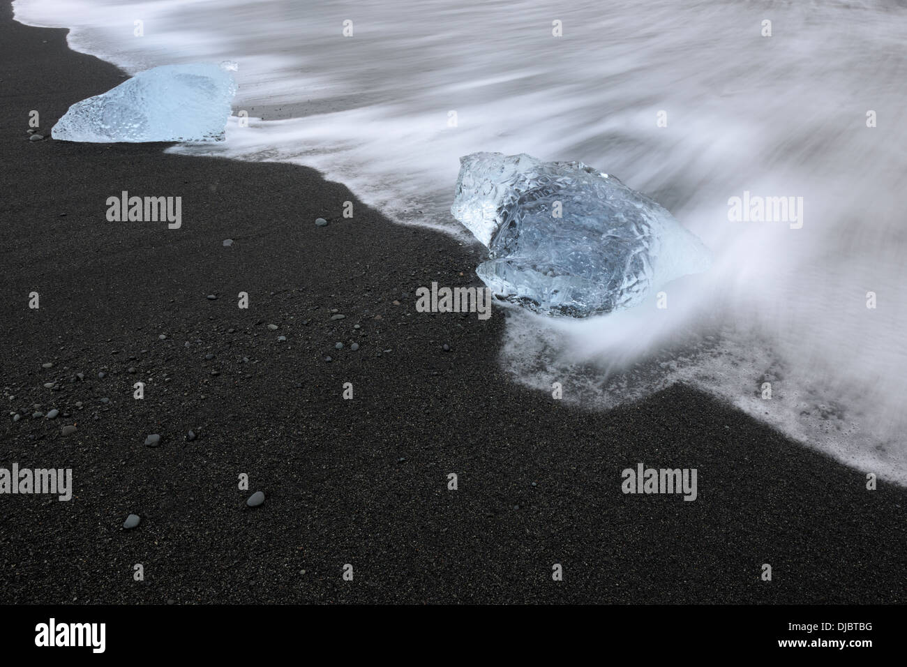 Bloc de glace sur une plage avec de l'eau et des pierres de lave flottant au-dessus. Banque D'Images