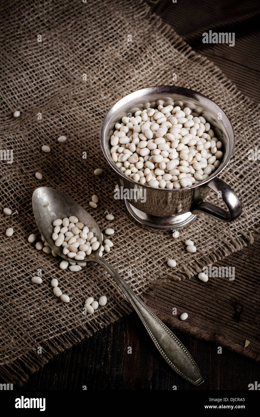 Haricots blancs secs dans une tasse de métal avec cuillère sur tissu du jute, studio shot Banque D'Images