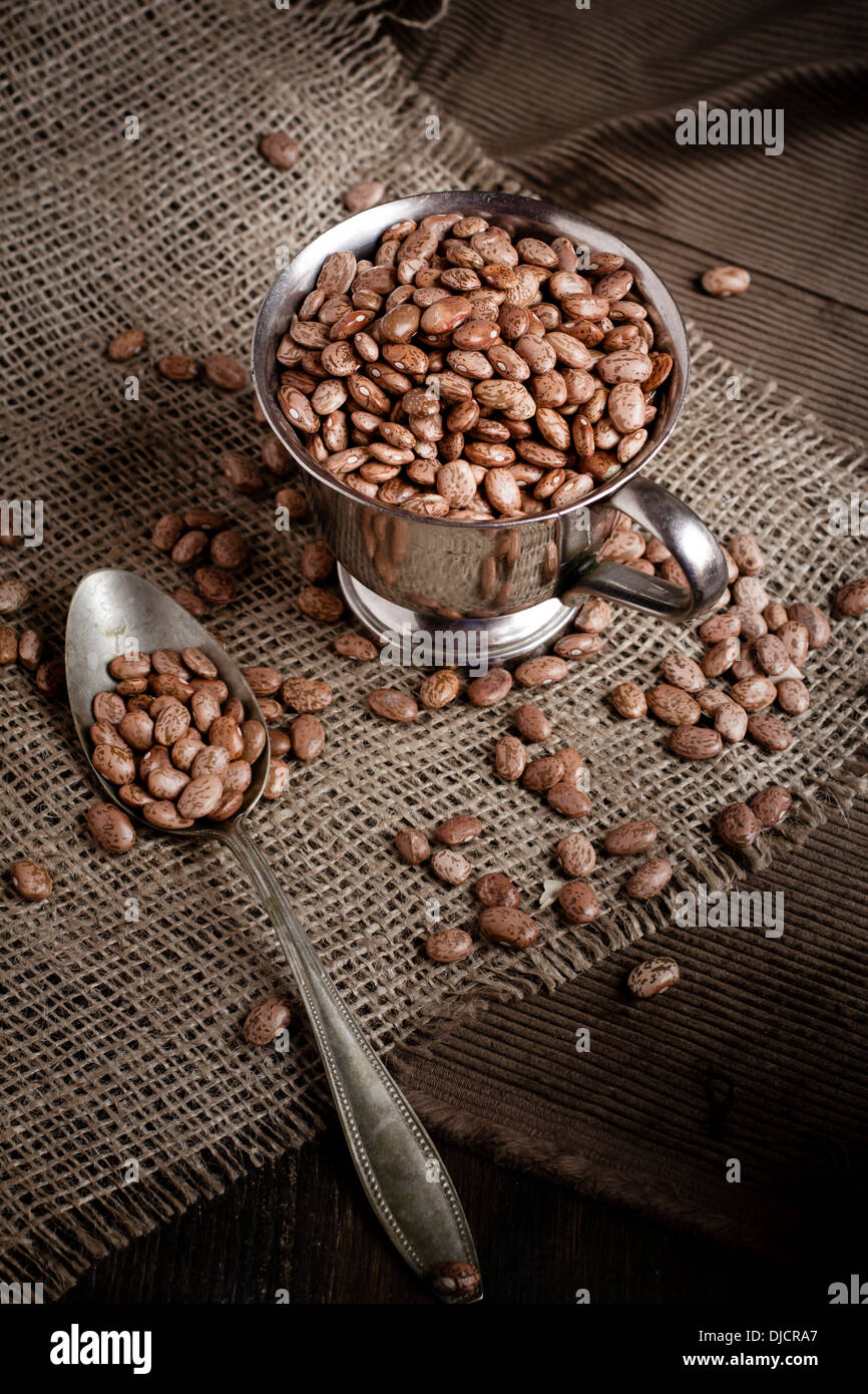 Haricots secs borlotti dans un gobelet de métal avec cuillère sur tissu du jute, studio shot Banque D'Images