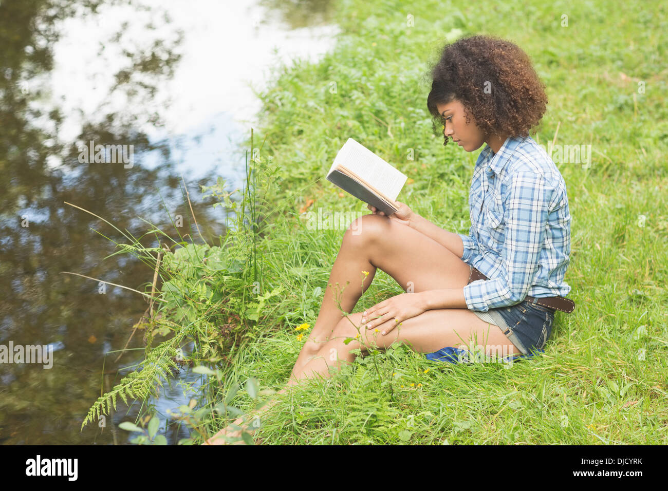 Calme superbe brunette sitting par un flux reading book Banque D'Images
