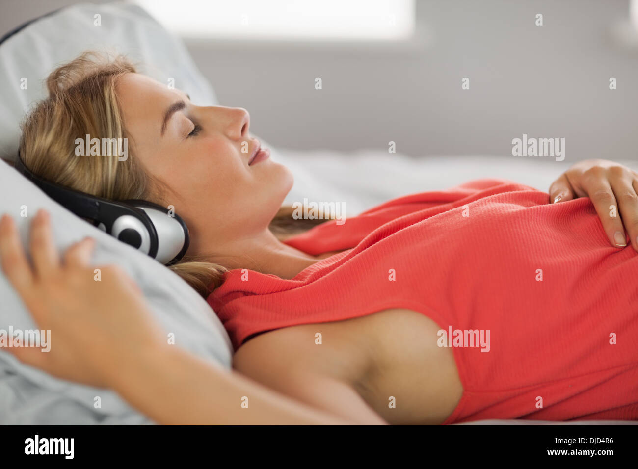 Peaceful blonde wearing dress lying on bed listening to music Banque D'Images
