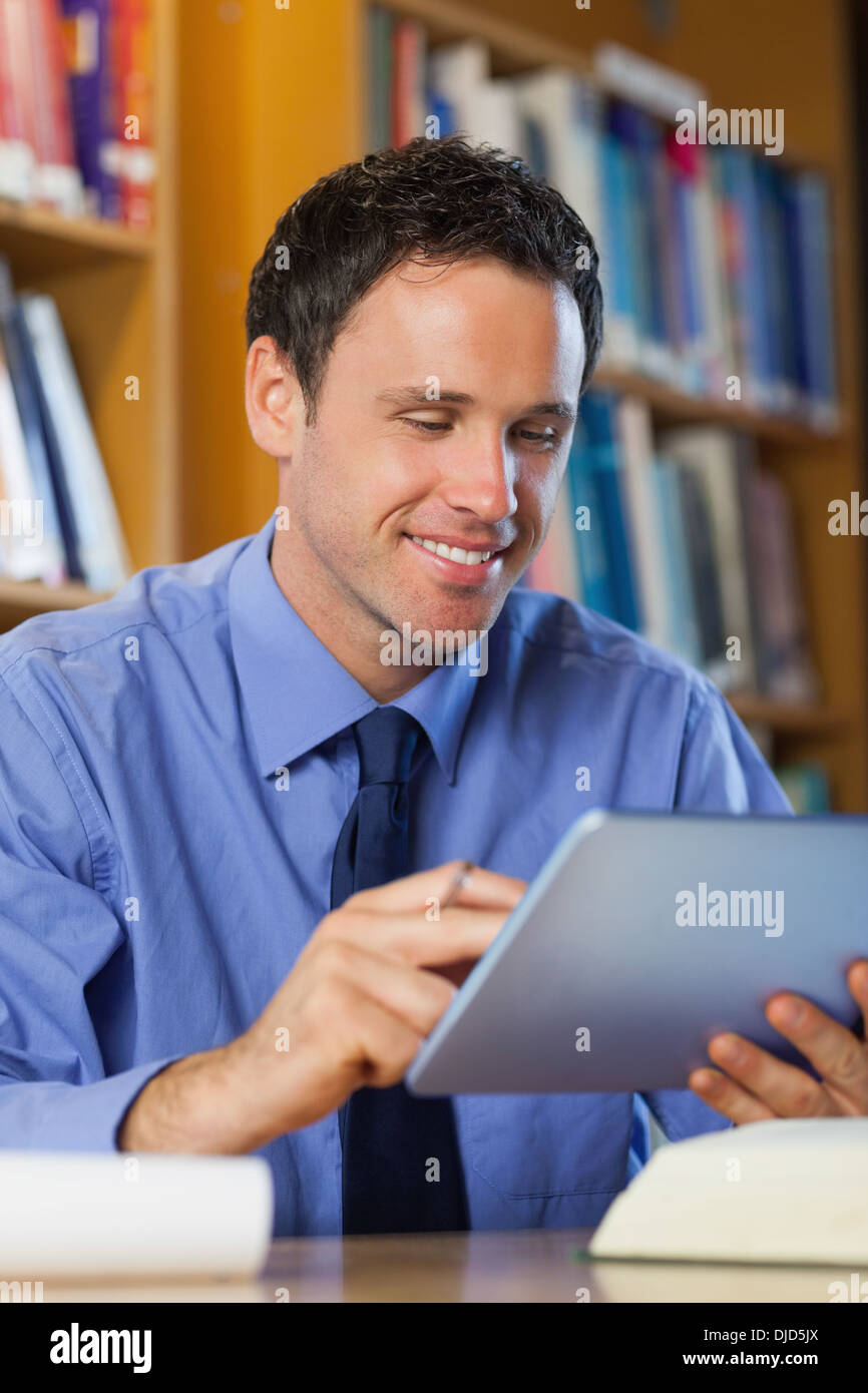 Bibliothécaire gaie sitting at desk using tablet Banque D'Images