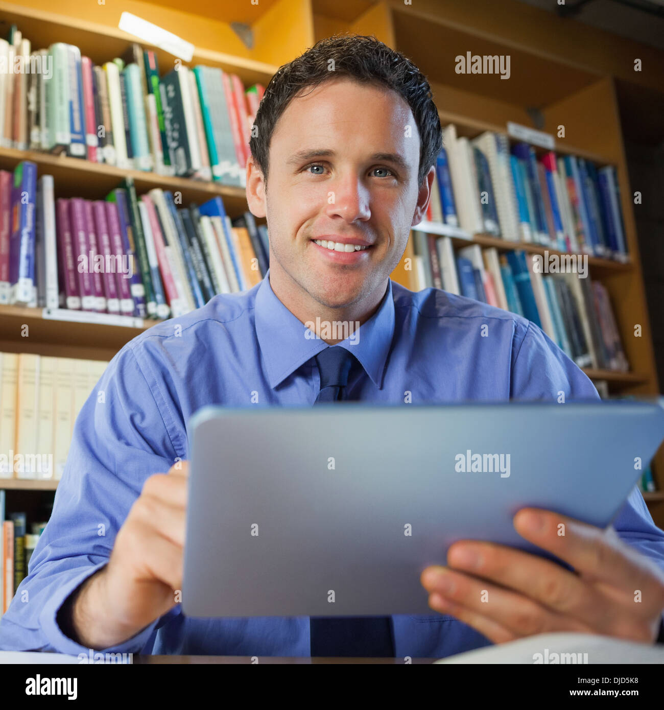 Bibliothécaire beau sitting at desk using tablet Banque D'Images
