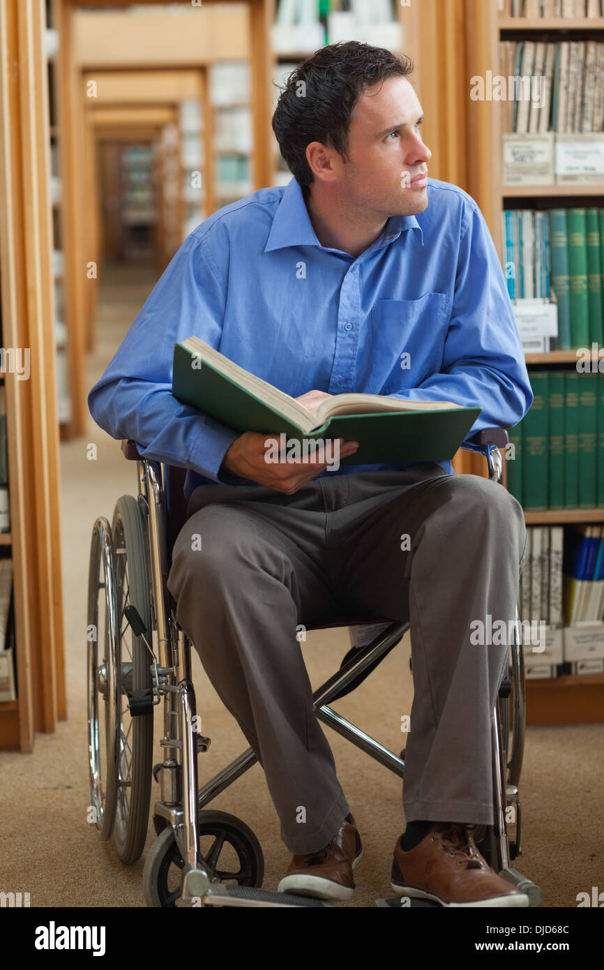Thoughtful man in wheelchair holding a book Banque D'Images