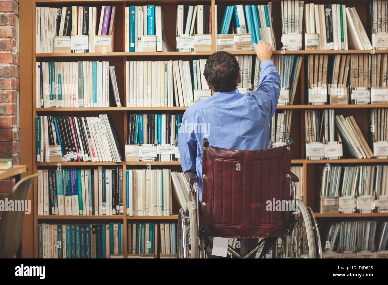 L'homme en fauteuil roulant en tenant un livre de bibliothèque Banque D'Images