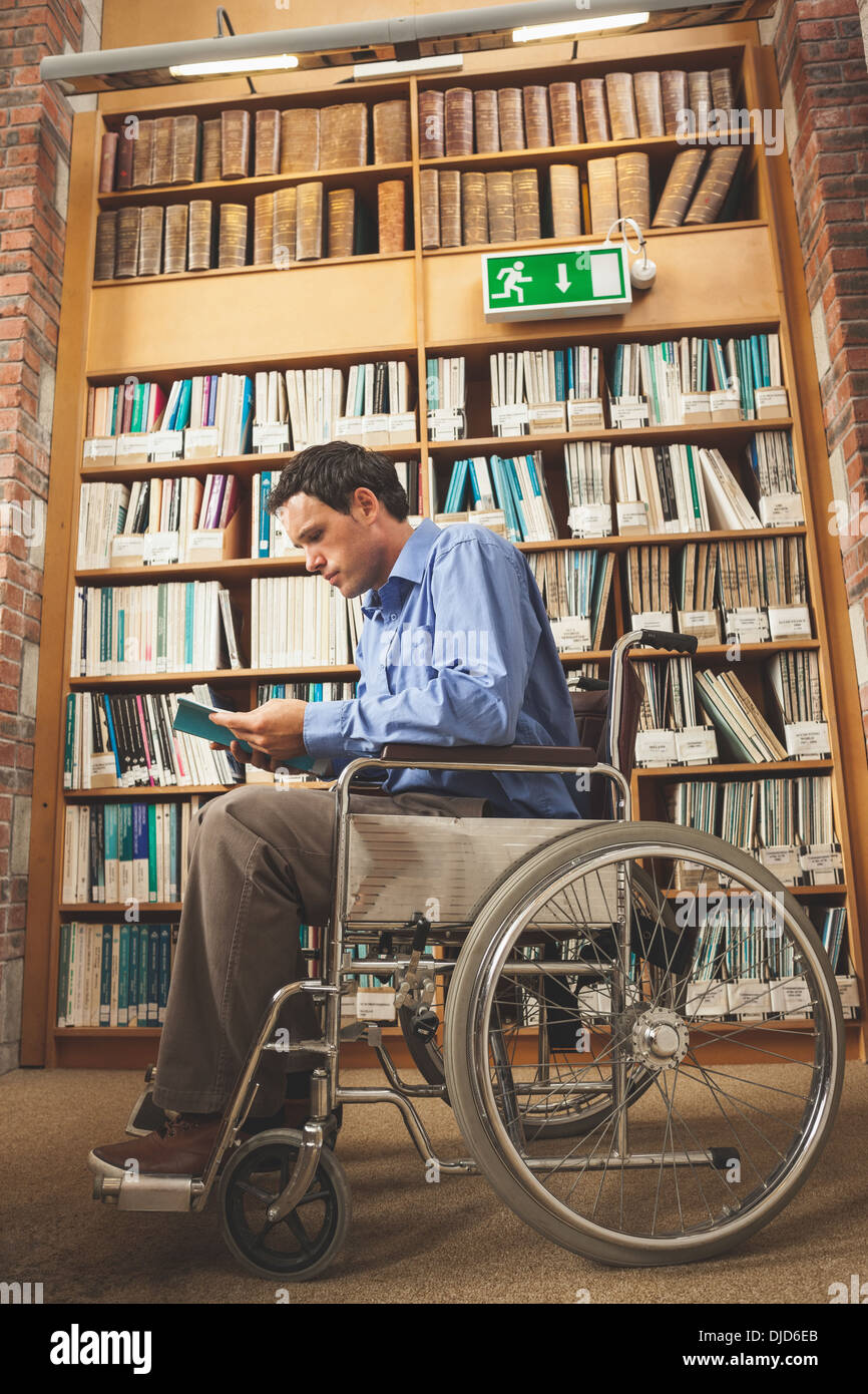 Fronçant man sitting in wheelchair reading a book Banque D'Images