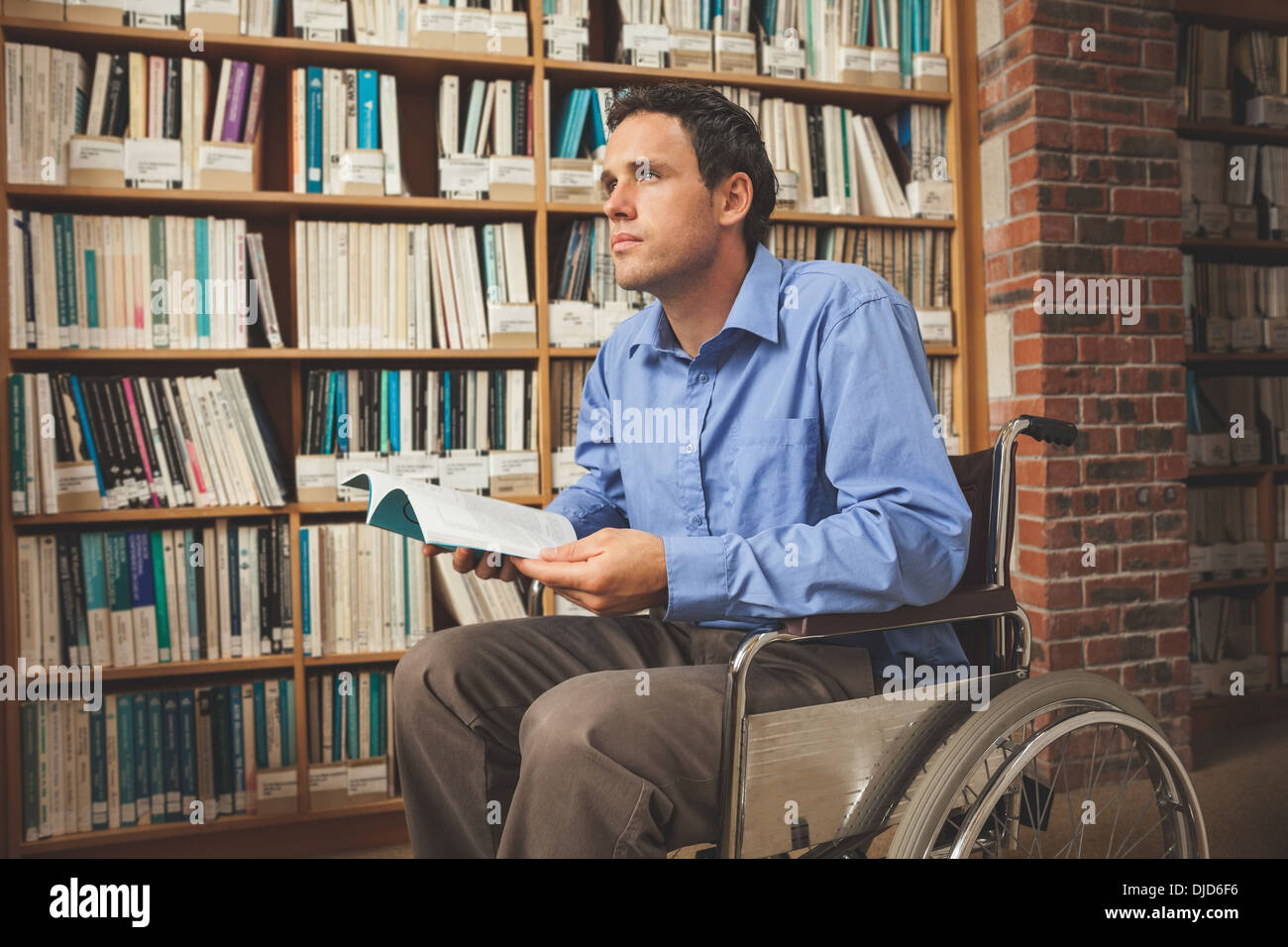 Thoughtful man sitting in wheelchair holding a book Banque D'Images