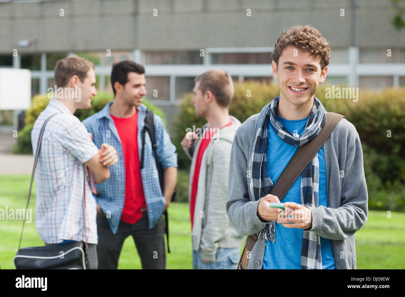 Cheerful male student l'envoi d'un texte en face de ses camarades à l'extérieur Banque D'Images