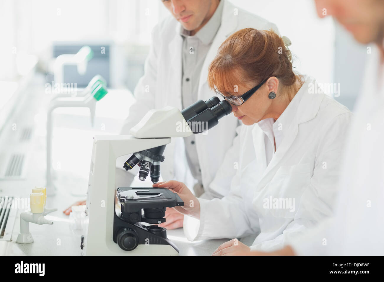 Femme debout regardant par microscope Banque D'Images