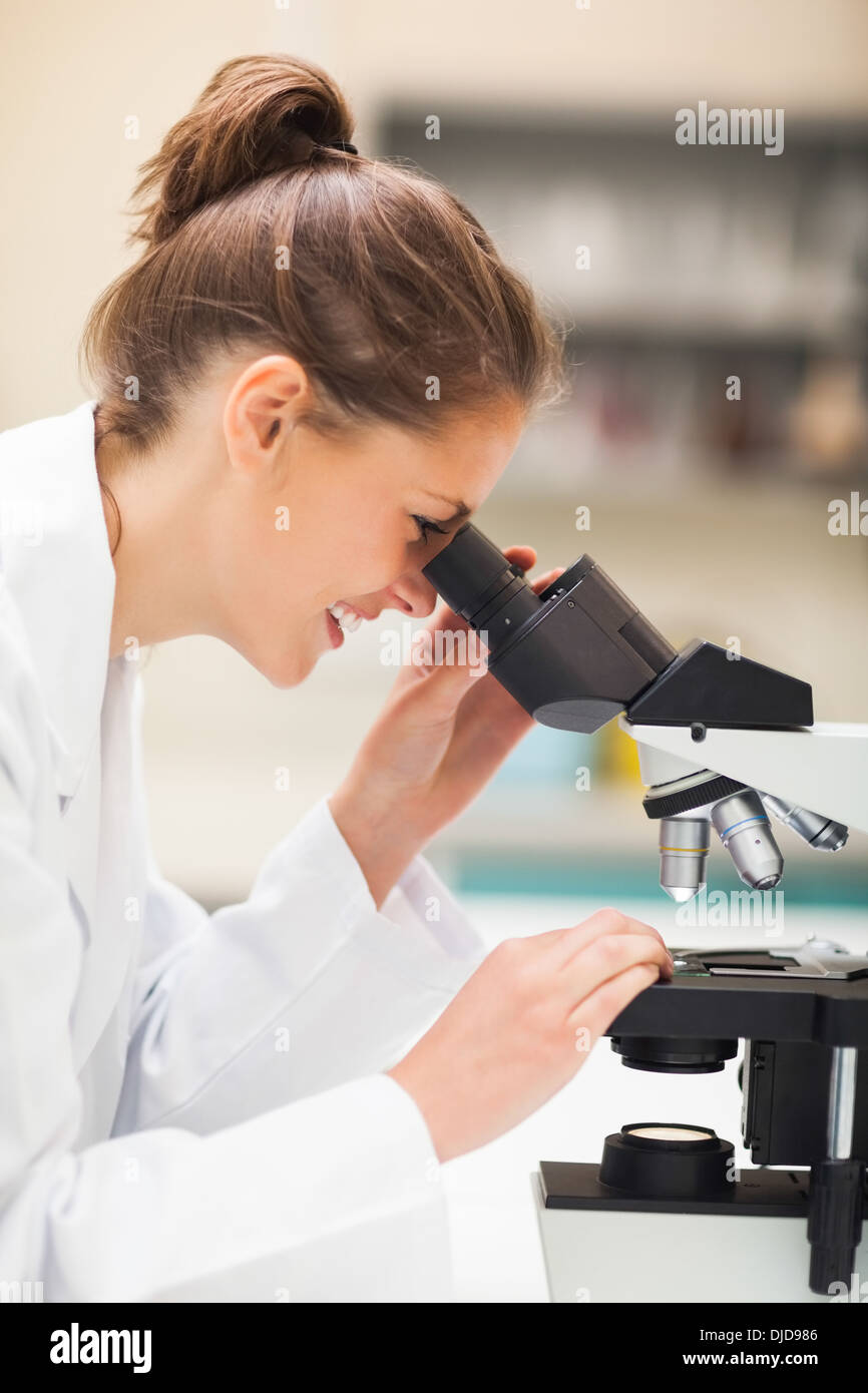 Cheerful brunette student microscope regardant à travers Banque D'Images