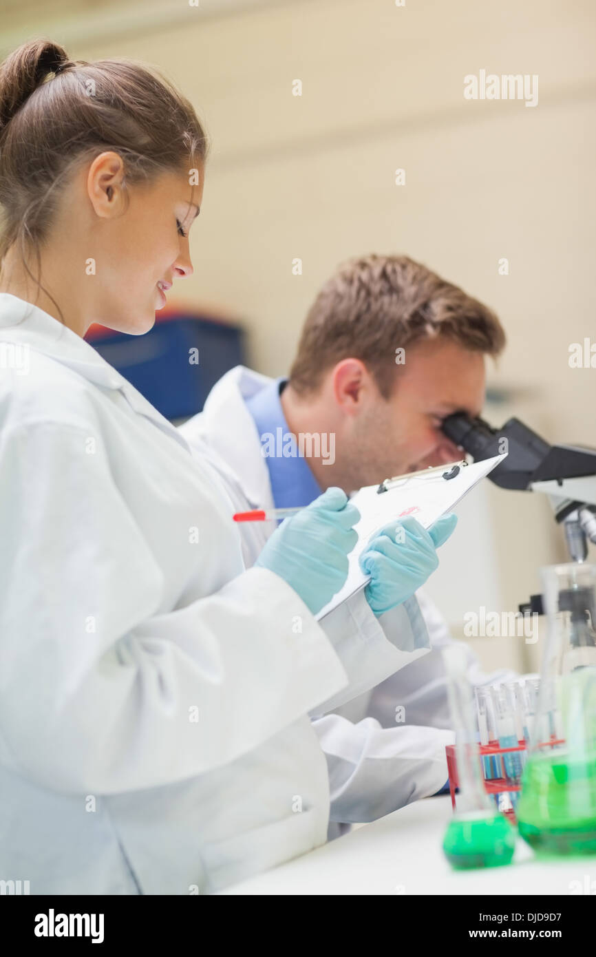 Deux étudiants à la recherche par microscope souriant et prendre des notes Banque D'Images