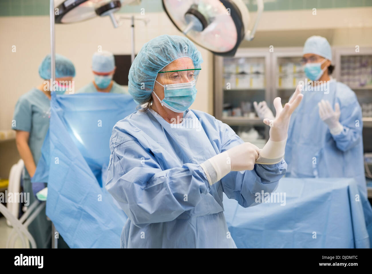 Médecin portant des gants chirurgicaux avec équipe en arrière-plan Banque D'Images