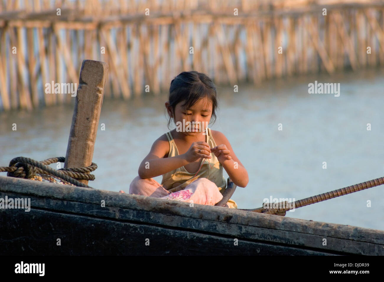 Un youing fille est assis dans un bateau de pêche près d'un pont de bambou sur la rivière du Mékong à Kampong Cham, au Cambodge. Banque D'Images