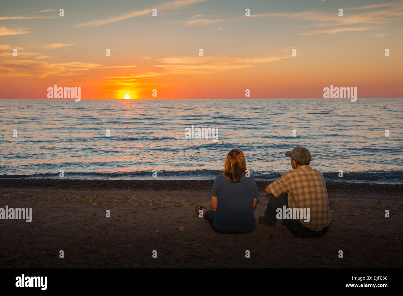 Un homme et une femme s'asseoir sur une plage en regardant le coucher du soleil sur le lac Érié, Presque Isle State Park ; Erie, Pennsylvanie Banque D'Images