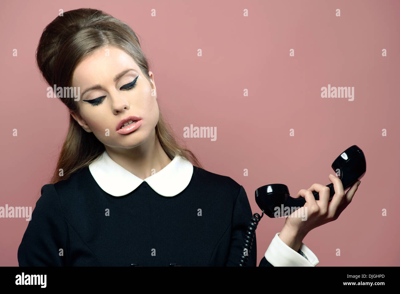 Une belle femme en robe vintage fermer les yeux maintenant un récepteur téléphonique vintage. Banque D'Images