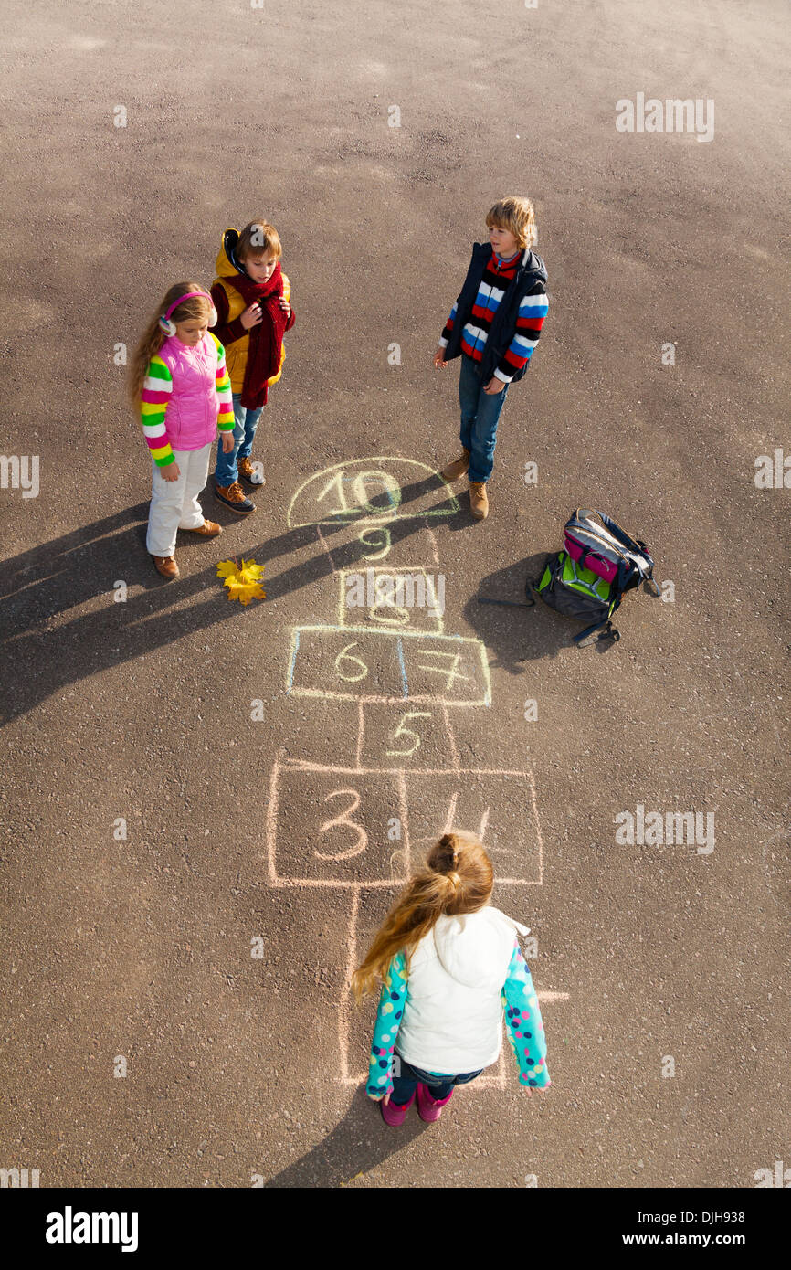 Groupe d'enfants sautant sur le jeu de marelle dessiné sur l'asphalte après l'école avec des vêtements d'automne Banque D'Images