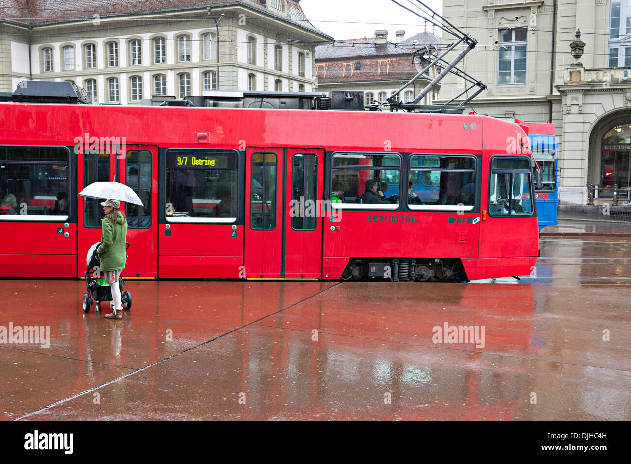 Femme debout dans la pluie holding up parapluie avec tramway rouge en arrière-plan, Berne Suisse Banque D'Images