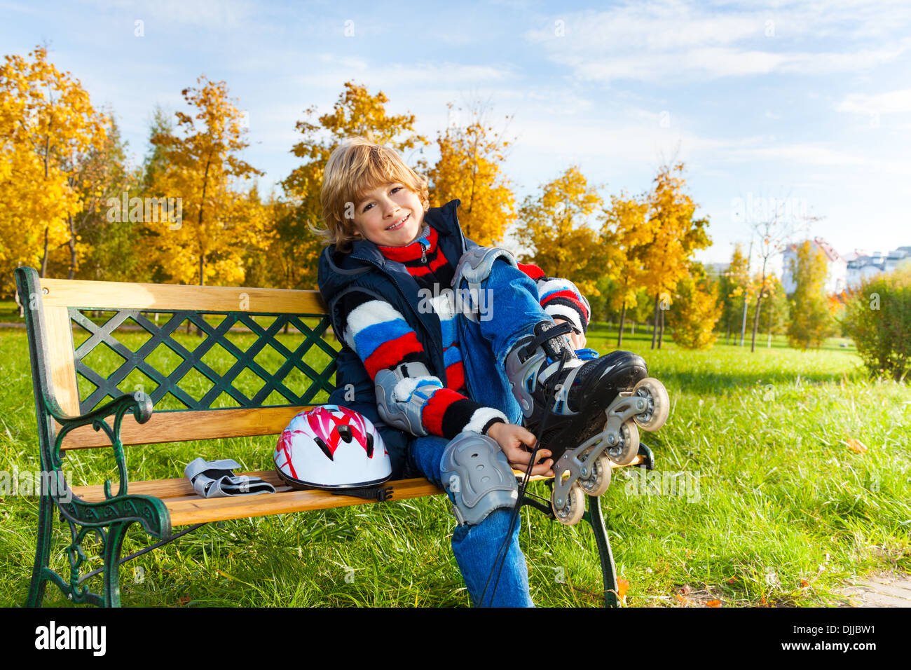 Happy blonde boy putting sur patins à assis sur le banc du parc en automne sur sunny day Banque D'Images