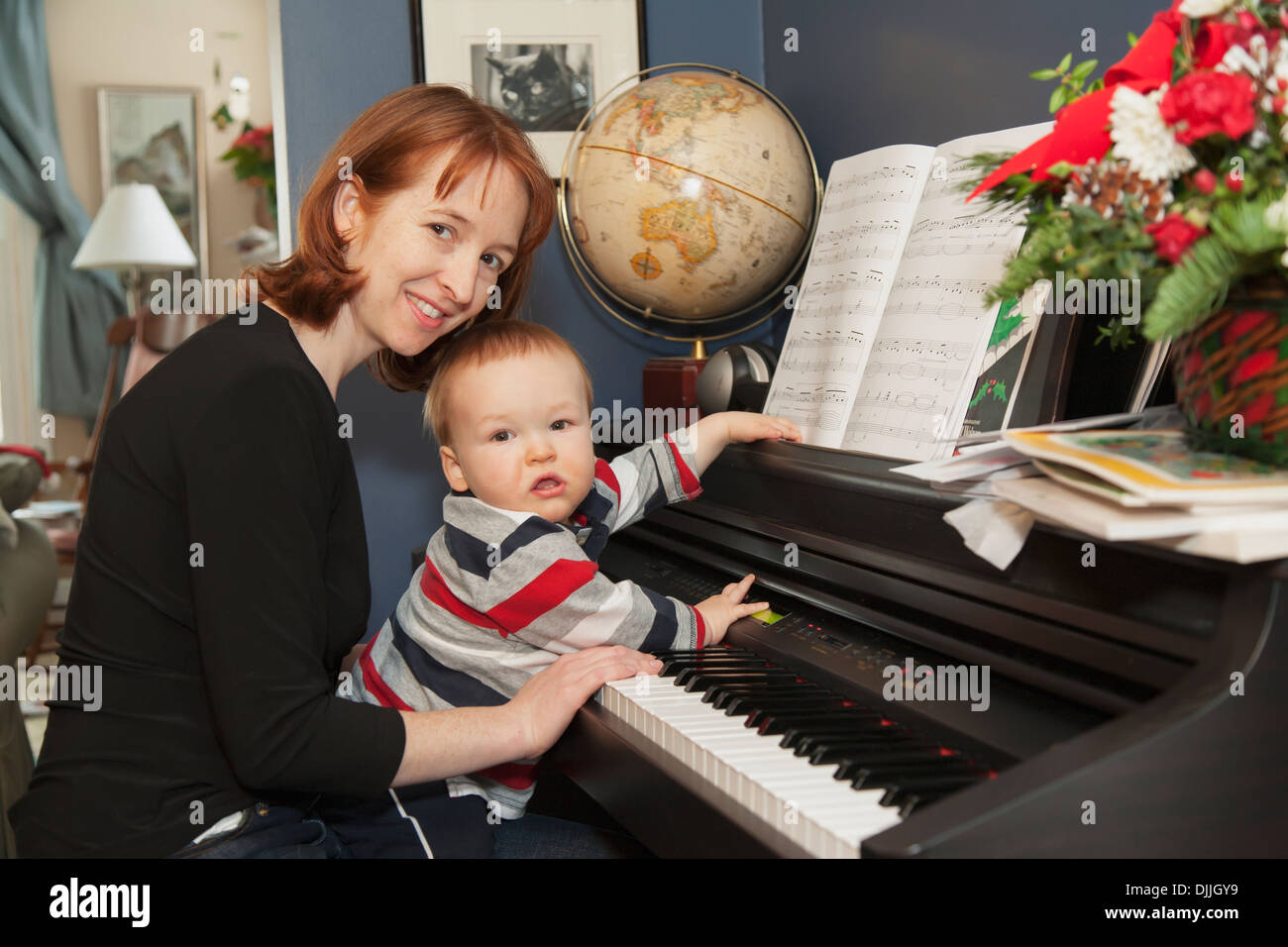 Un garçon de 15 mois est assis sur les genoux de sa mère alors qu'elle l'aide à jouer un piano électronique dans leur maison Banque D'Images