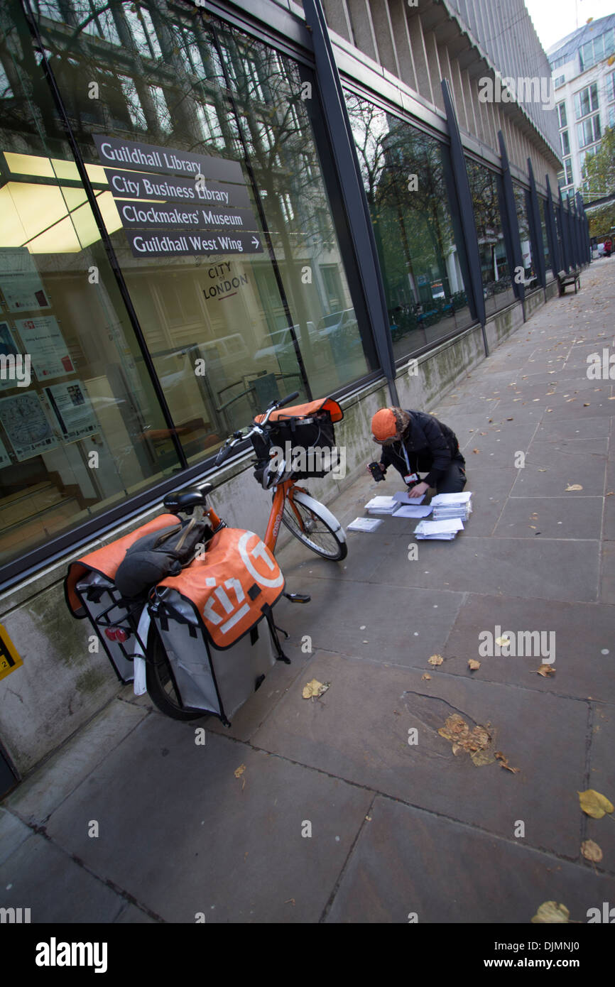 Femme TNT courrier à cycle postal en uniforme avec le courrier de tri de bicyclette de marque sur le trottoir dans le centre de Londres, Royaume-Uni. Service de livraison urbaine en action. Banque D'Images