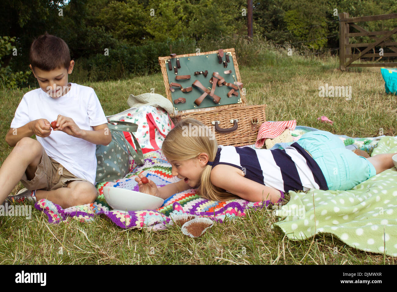 Les enfants à un pique-nique de manger de la nourriture et de s'amuser dans l'herbe longue à Somerset, Royaume-Uni. Banque D'Images