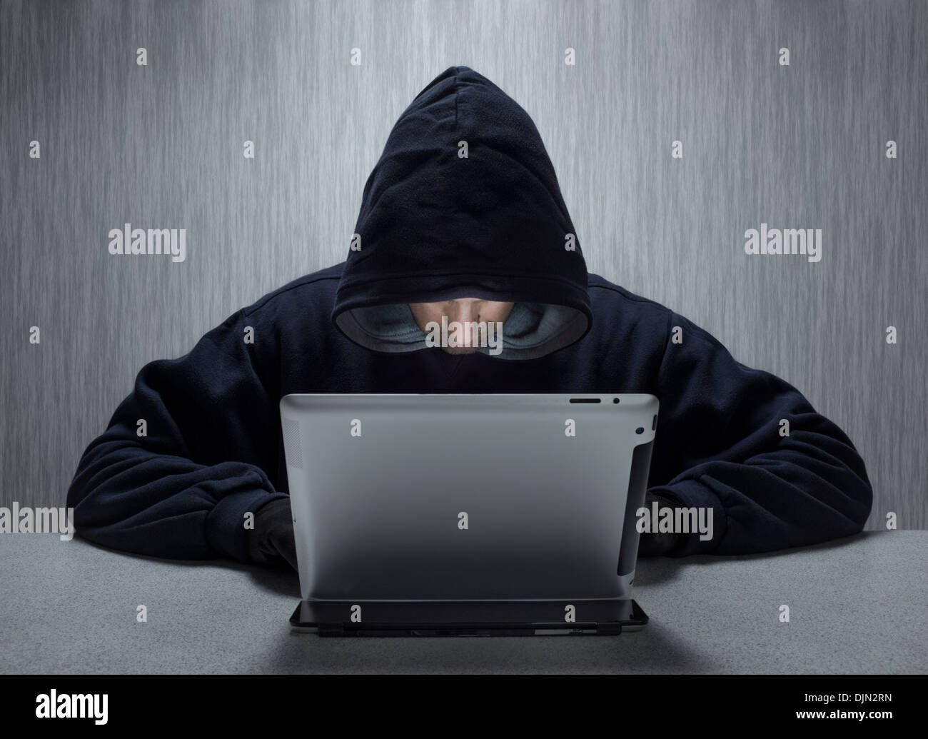 Un capuchon à l'aide d'un homme anonyme ordinateur tablette représentant un cyber criminel. Banque D'Images