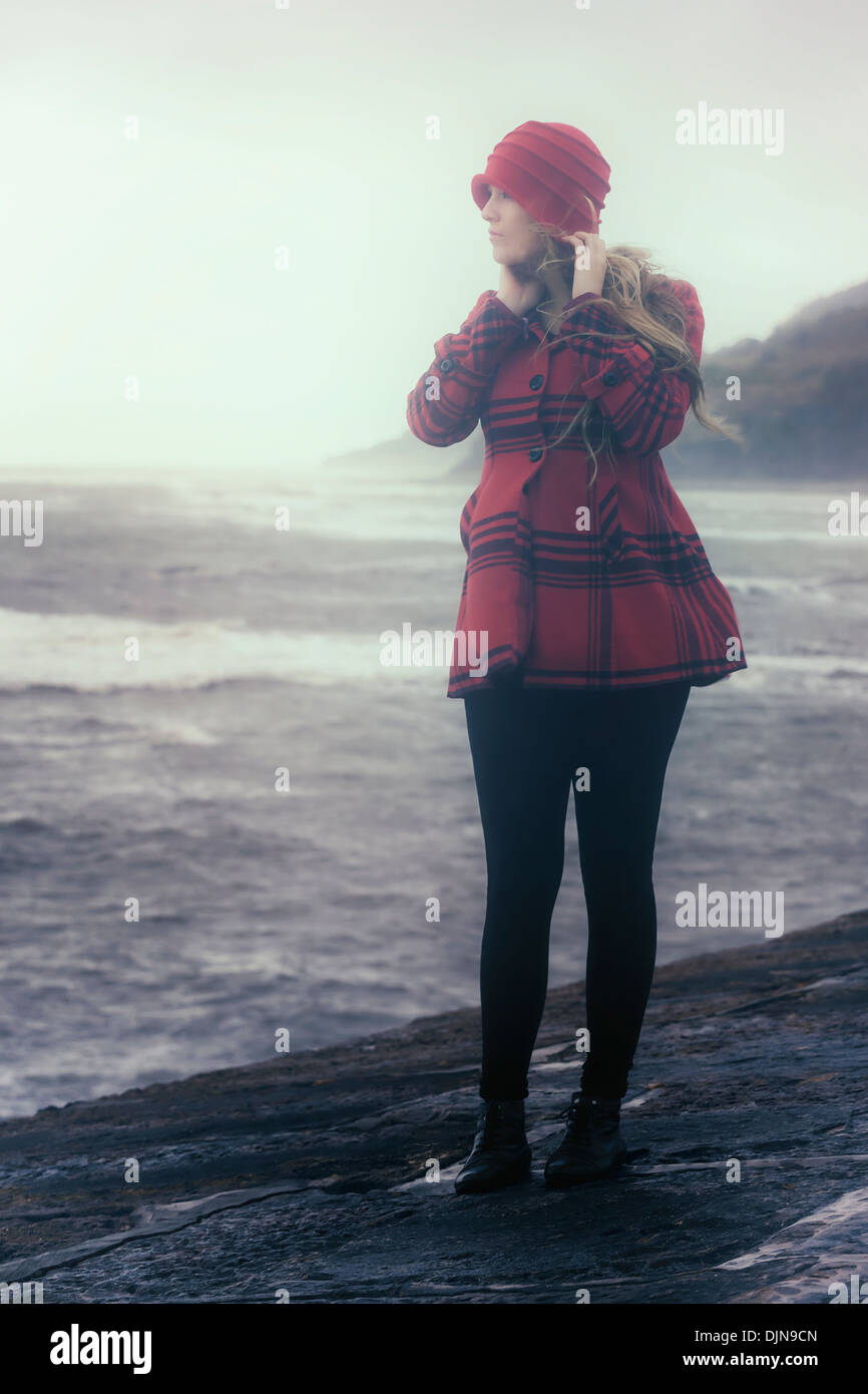 Une femme dans un manteau rouge est debout sur un vieux quai en pierre Banque D'Images