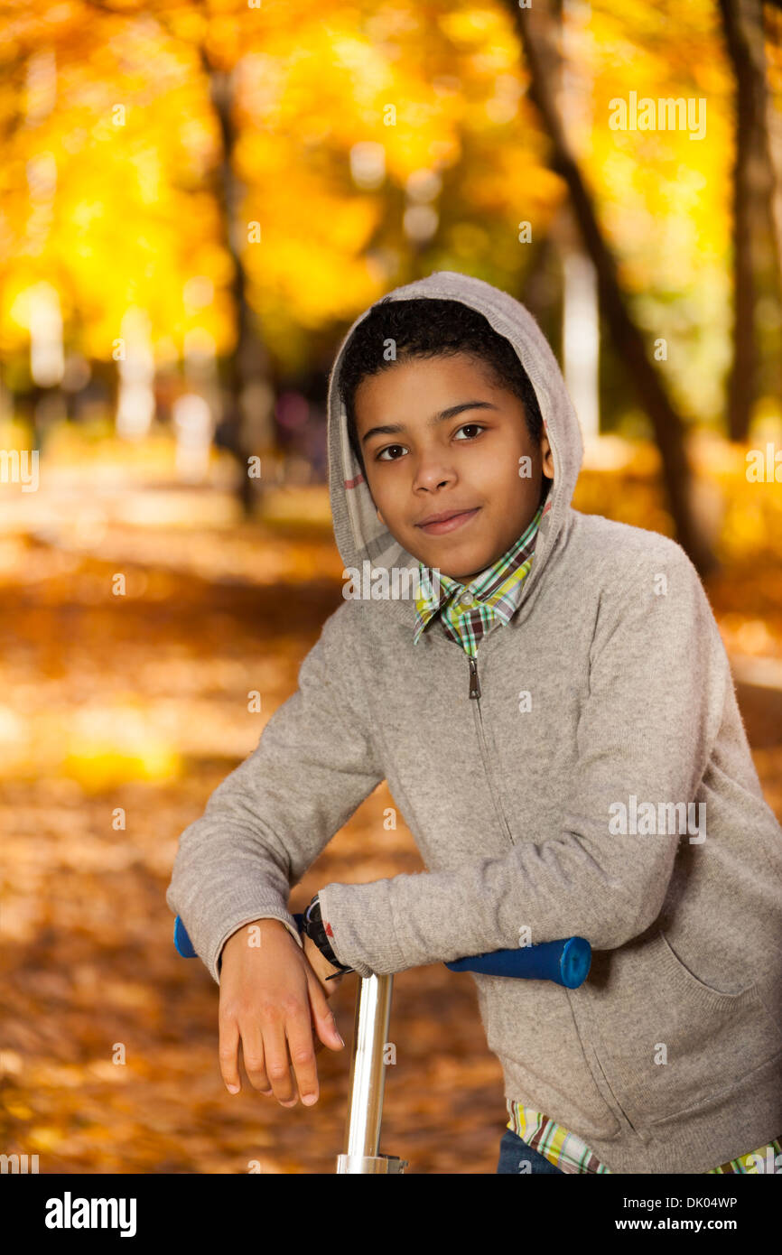 Fermer portrait beau black 10 ans boy riding a scooter en automne avec les feuilles d'érable orange park Banque D'Images