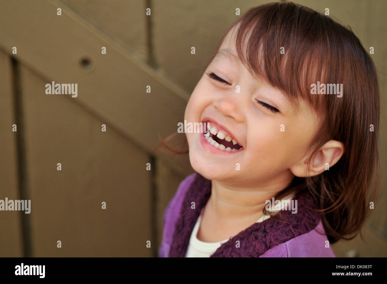 Un enfant de deux ans M. mixed race female rit tout en ayant sa photo prise. Elle a les cheveux bruns et porte une chemise violette. Banque D'Images