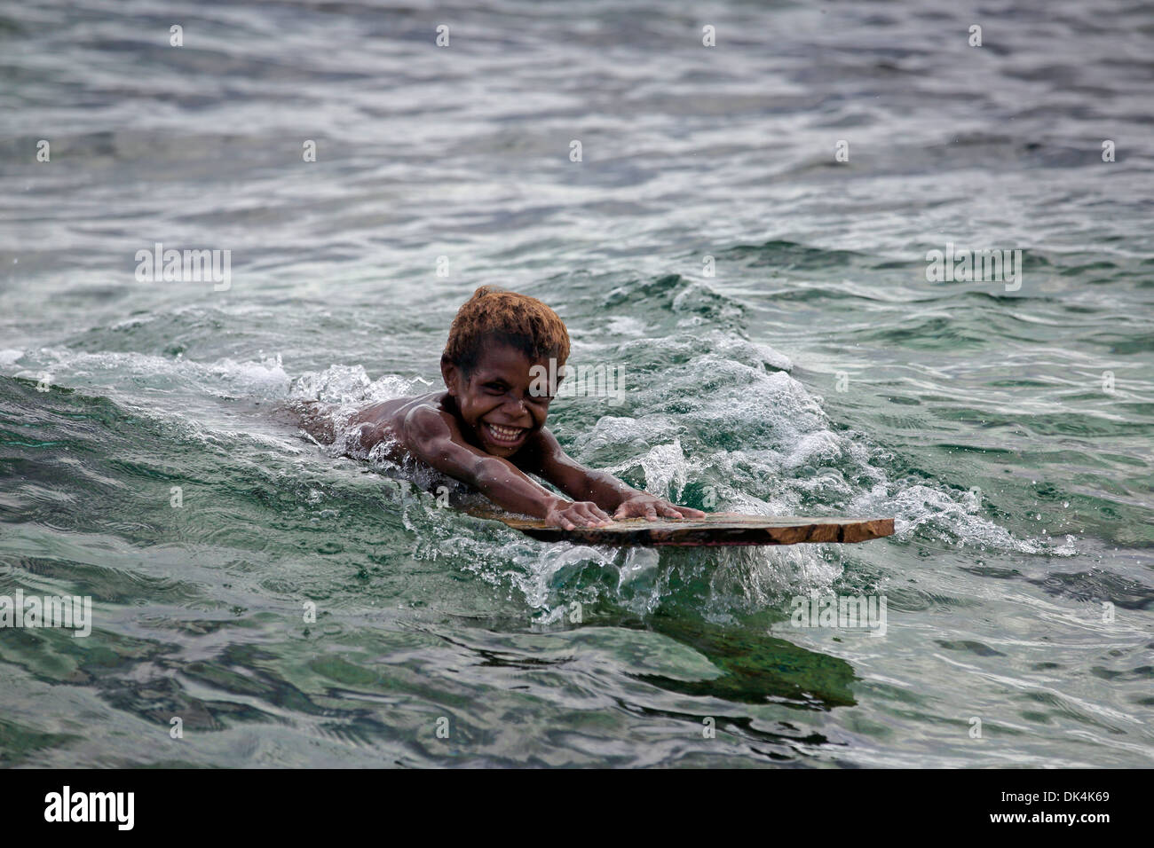 Young smiling boy papoue surf sur morceau de bois sur la côte Pacifique près de Manokwari en Papouasie Occidentale Banque D'Images