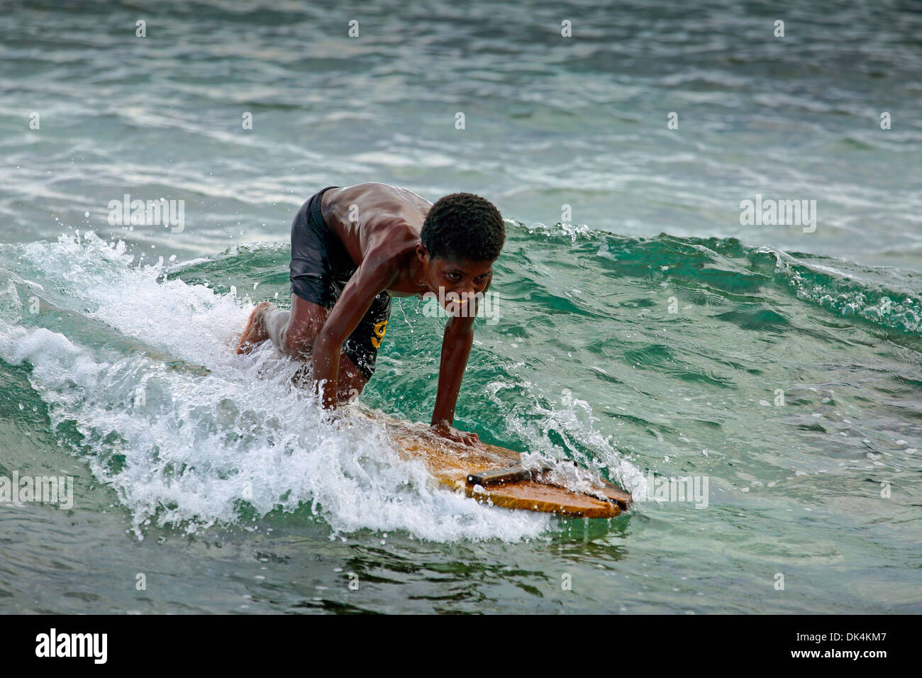 Young smiling boy papoue surf sur morceau de bois sur la côte Pacifique près de Manokwari en Papouasie Occidentale Banque D'Images