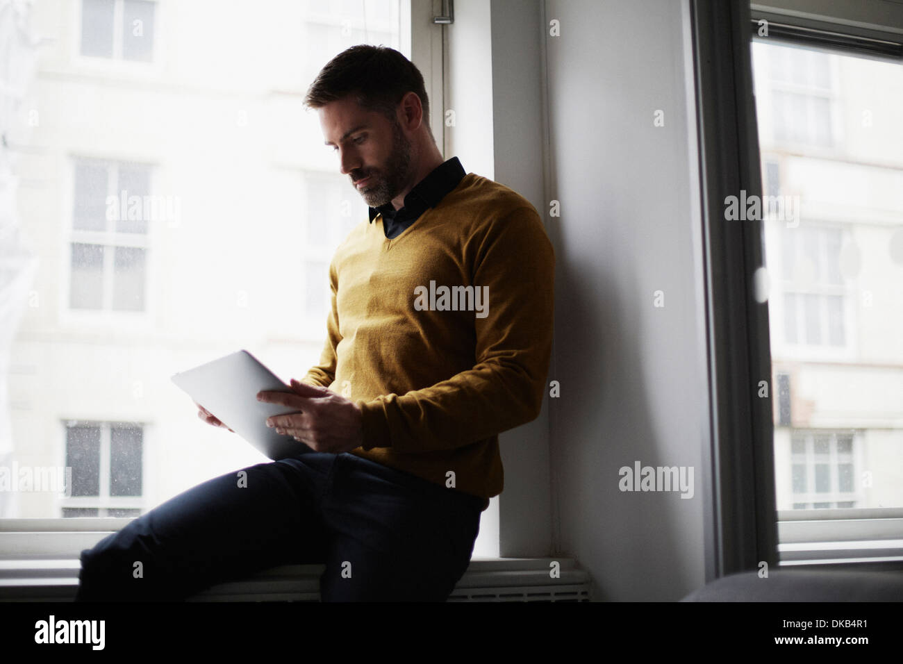 Businessman sitting on windowsill using digital tablet Banque D'Images