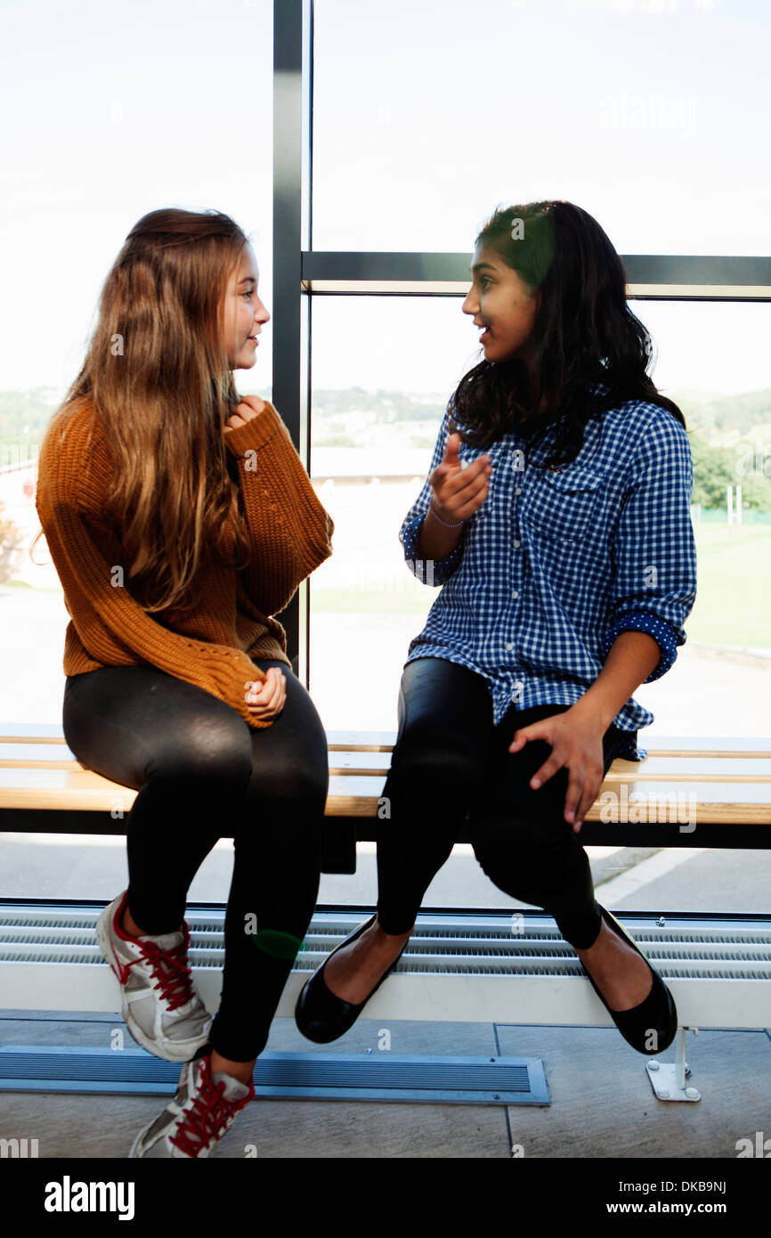 Deux jeunes écolières assis bavardant dans couloir Banque D'Images