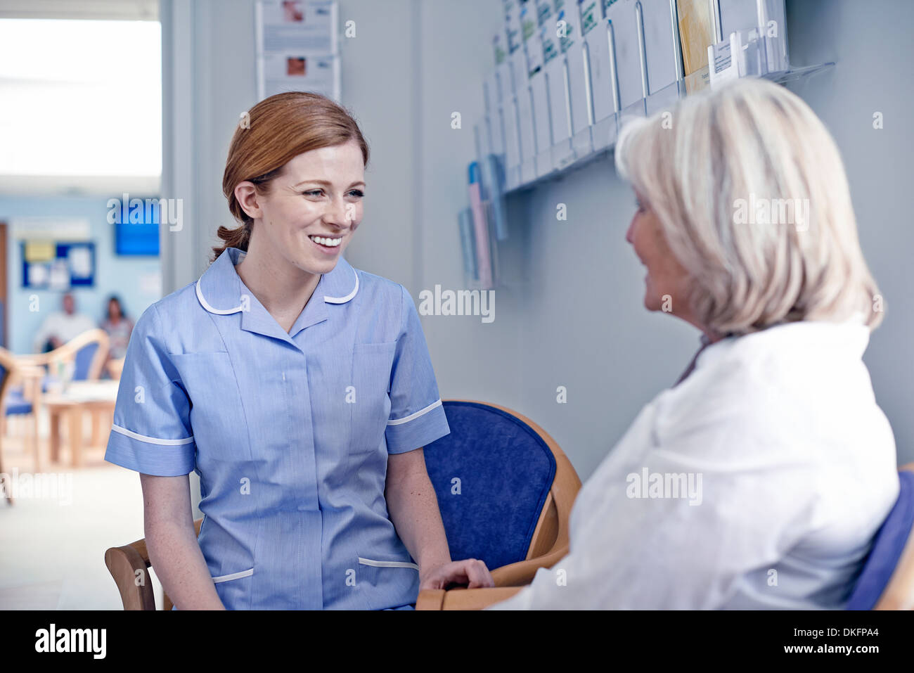 Femme assise avec nurse in hospital waiting room Banque D'Images