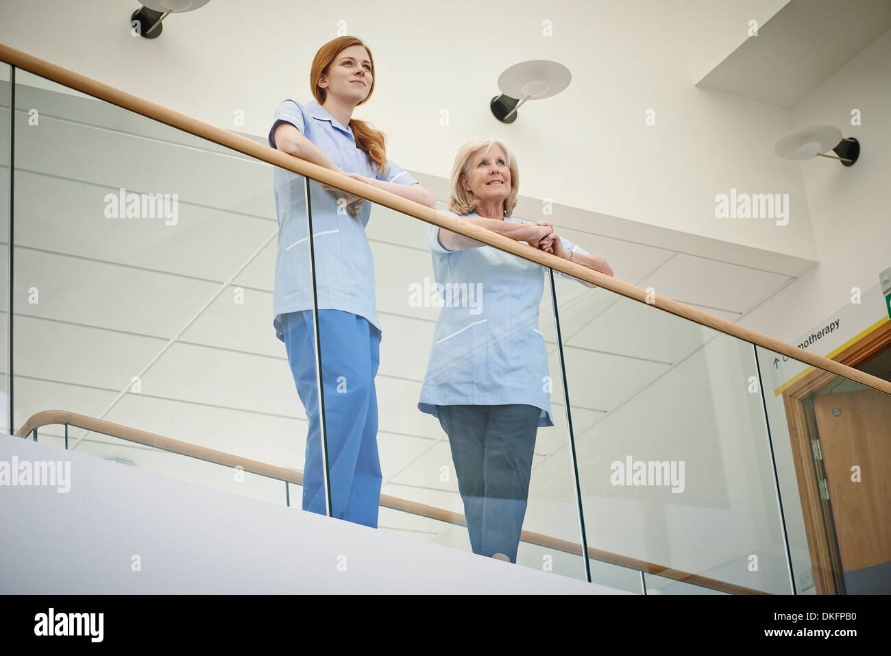Deux femmes en soins infirmiers en attente sur balcon atrium de l'hôpital Banque D'Images