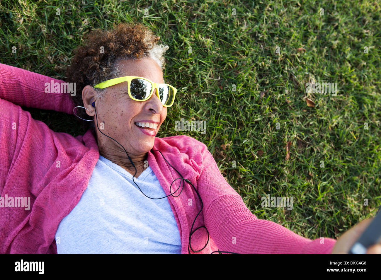 Portrait of senior woman lying on grass wearing sunglasses Banque D'Images