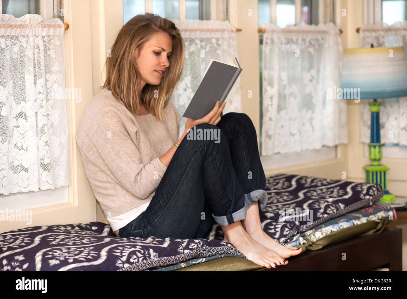 Young woman reading book in window seat Banque D'Images