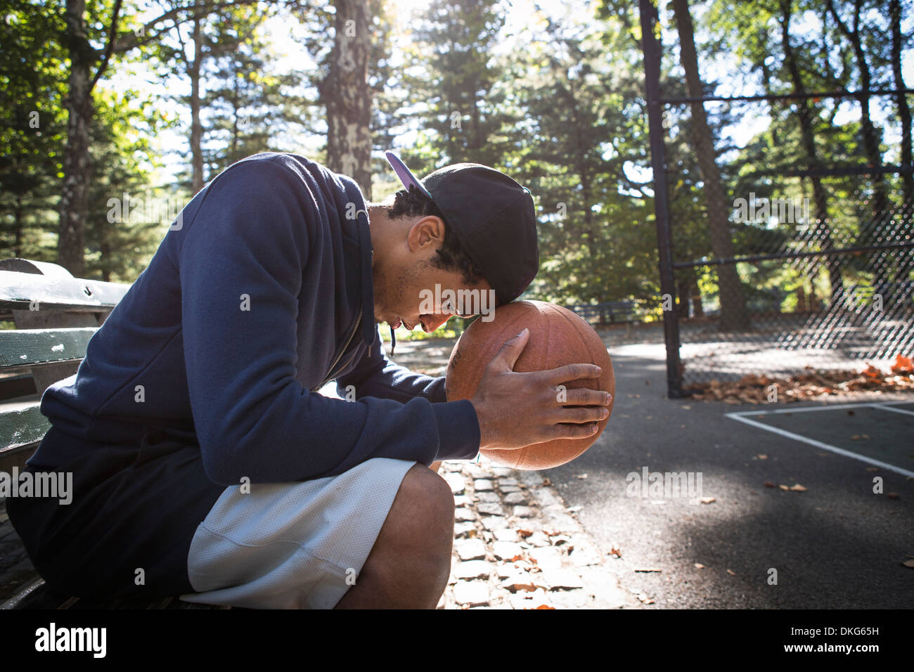 Jeune homme assis sur le banc de parc resting head on basketball Banque D'Images