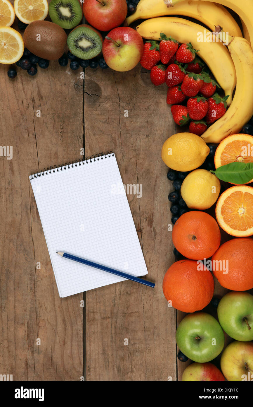 Des fruits comme les oranges, les bananes, les pommes et les citrons sur une planche en bois avec une liste d'achats Banque D'Images