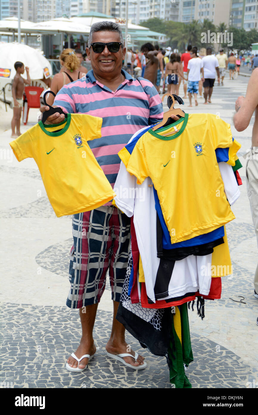 Un colporteur avec une brassée de maillots de football brésilien en vente sur la plage de Copacabana à Rio de Janeiro, Brésil Banque D'Images