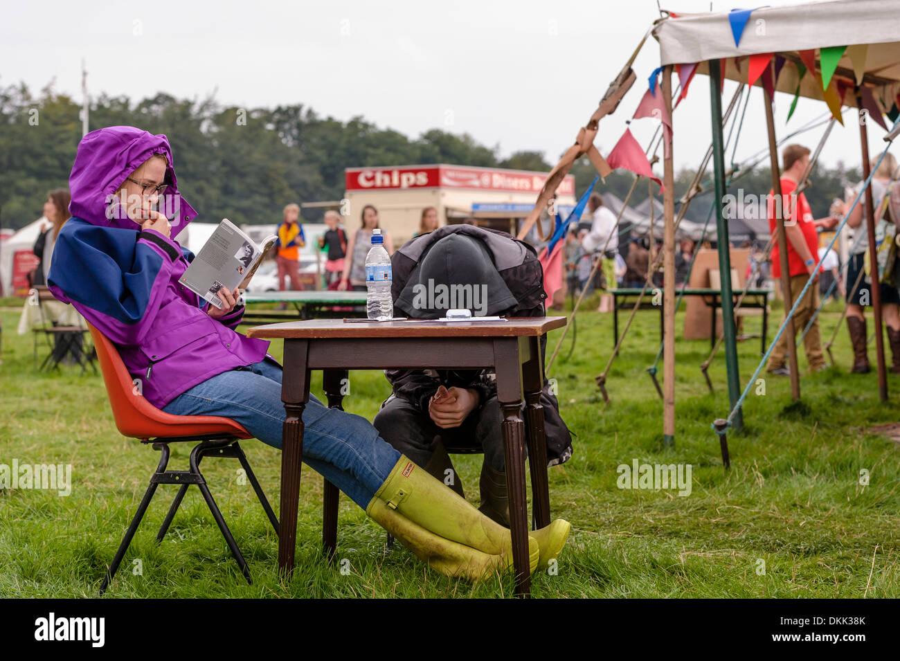 Un couple assis à une table à l'extérieur à un festival de musique. Le jeune homme a sa tête sur la table. La femme est la lecture. Banque D'Images