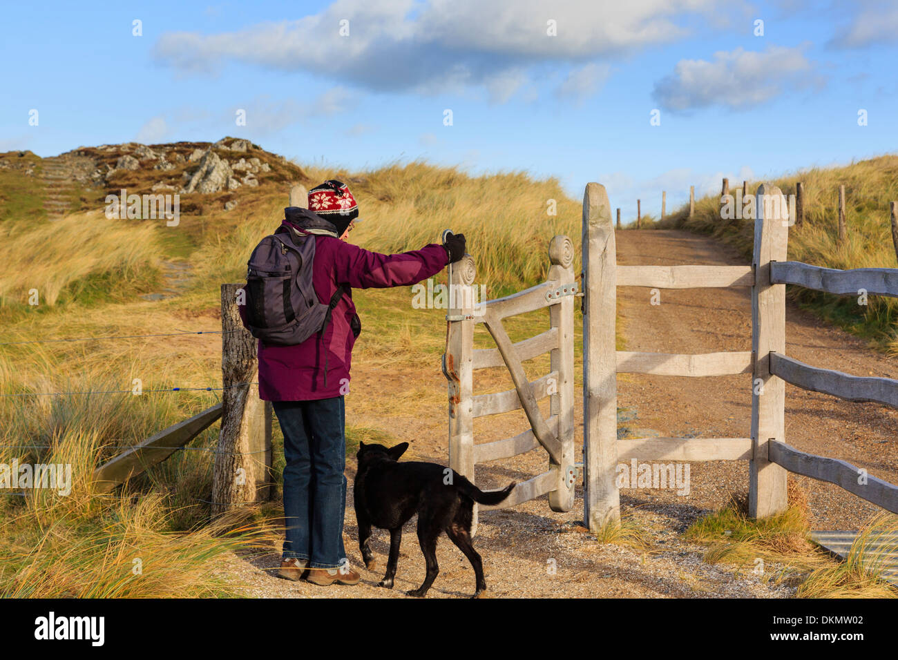 Un chien marche walker femme baiser d'ouverture porte sur chemin principal sur l'île Llanddwyn Ynys. Newborough Isle of Anglesey au nord du Pays de Galles UK Banque D'Images