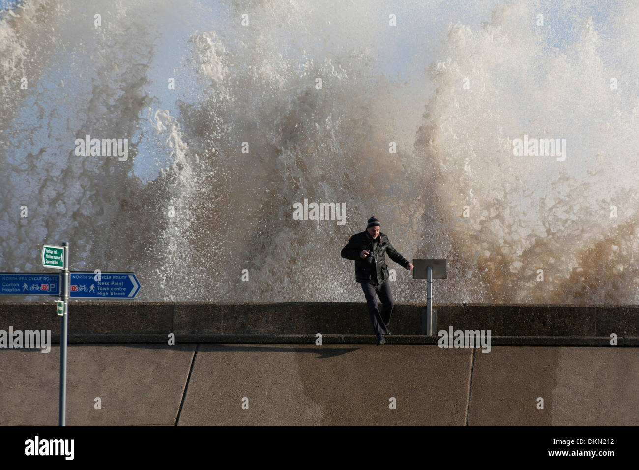 Lowestoft, UK. 06 Dec, 2013. Un photographe regarde la haute mer spectaculaire se briser contre le mur de la mer à Lowestoft. Le panneau bleu au premier plan indique que la mer mur fait partie de la mer du Nord Randonnée à Vélo et points à Lowestoft centre-ville. Elle mentionne également Ness Point qui est un peu plus loin le long de la digue, marquant l'endroit le plus à l'est au Royaume-Uni. Credit : Solveig Stibbe/Alamy Live News Banque D'Images