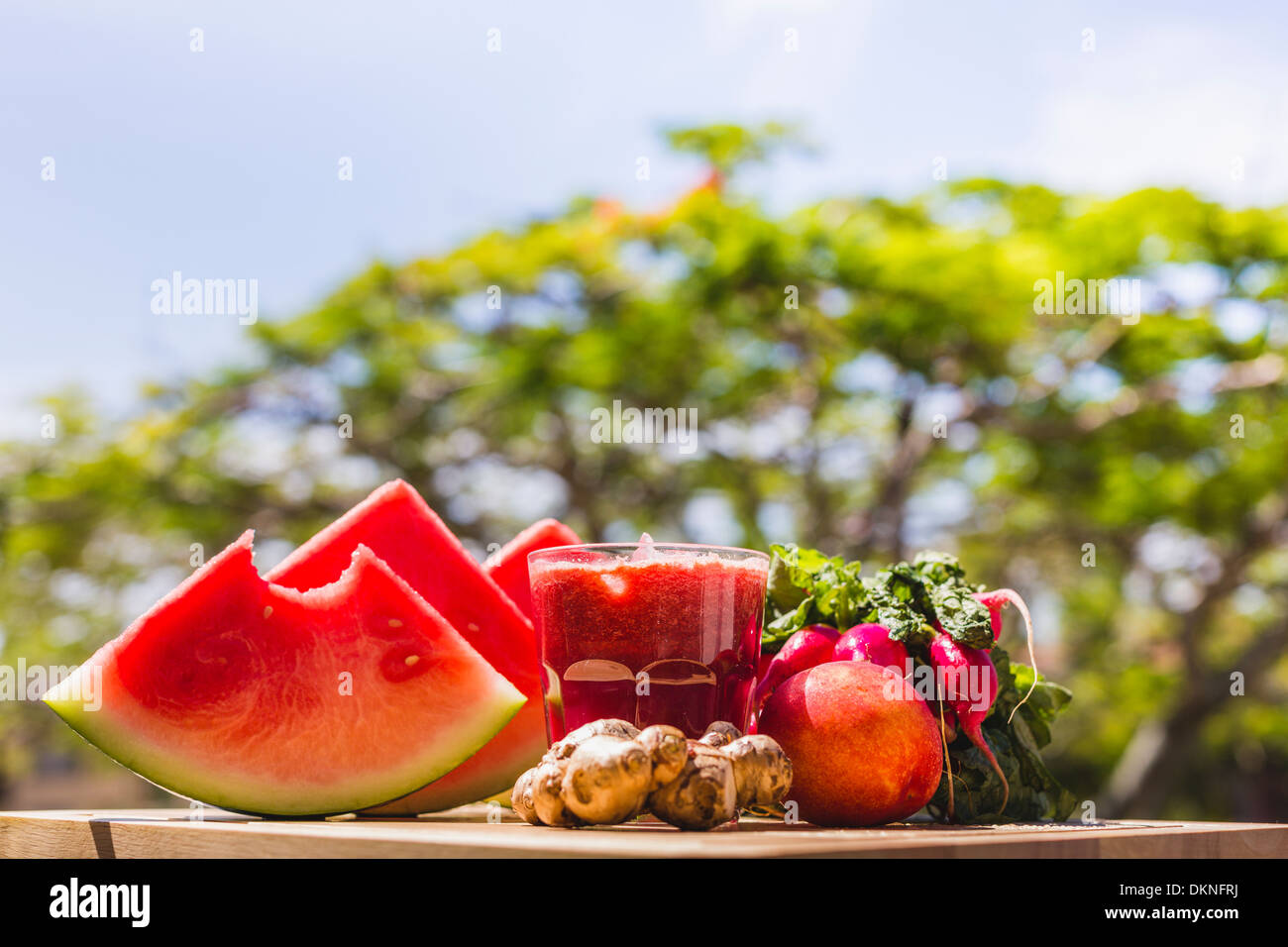 Jus frais et produire sur planche de bois avec la verdure en arrière-plan Banque D'Images