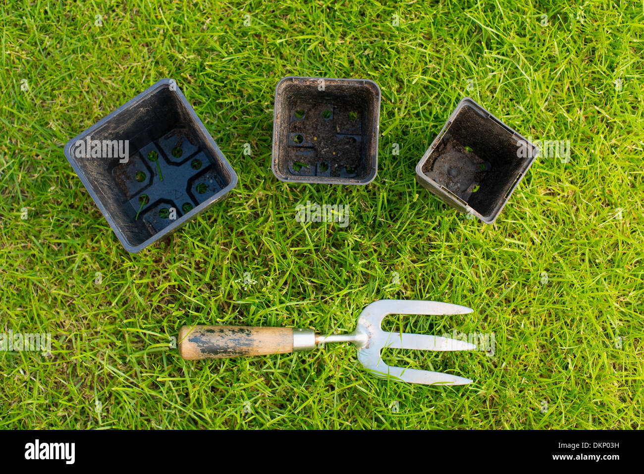 Trois pots utilisés noir et un jardin d'usure sur une fourche patch d'herbe vert clair Banque D'Images