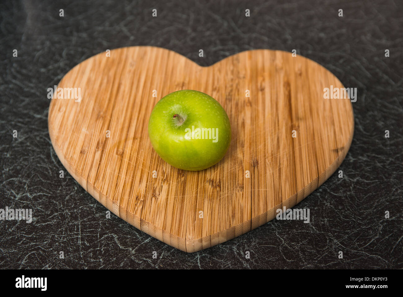 Une pomme verte lumineuse sur un coeur en bois planche à découper Banque D'Images