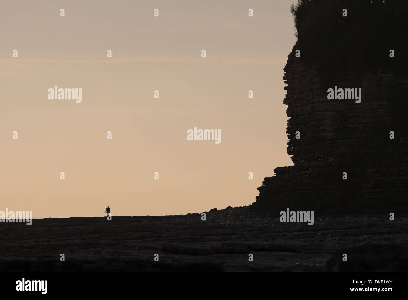 Silhouette solitaire lointain éclipsé par falaise massive au crépuscule Banque D'Images