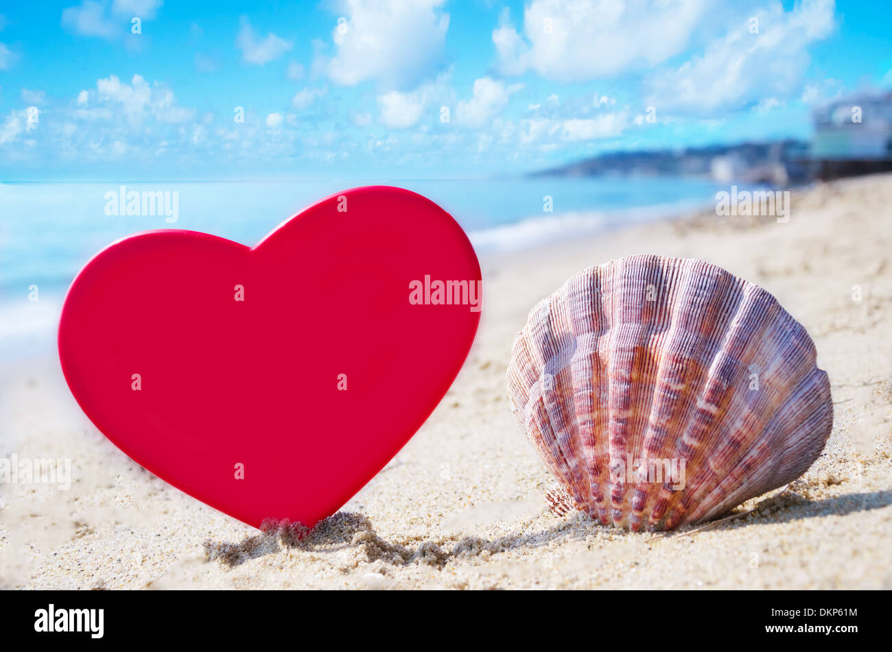 Forme de coeur et d'un coquillage sur une plage de sable à l'océan en journée ensoleillée Banque D'Images